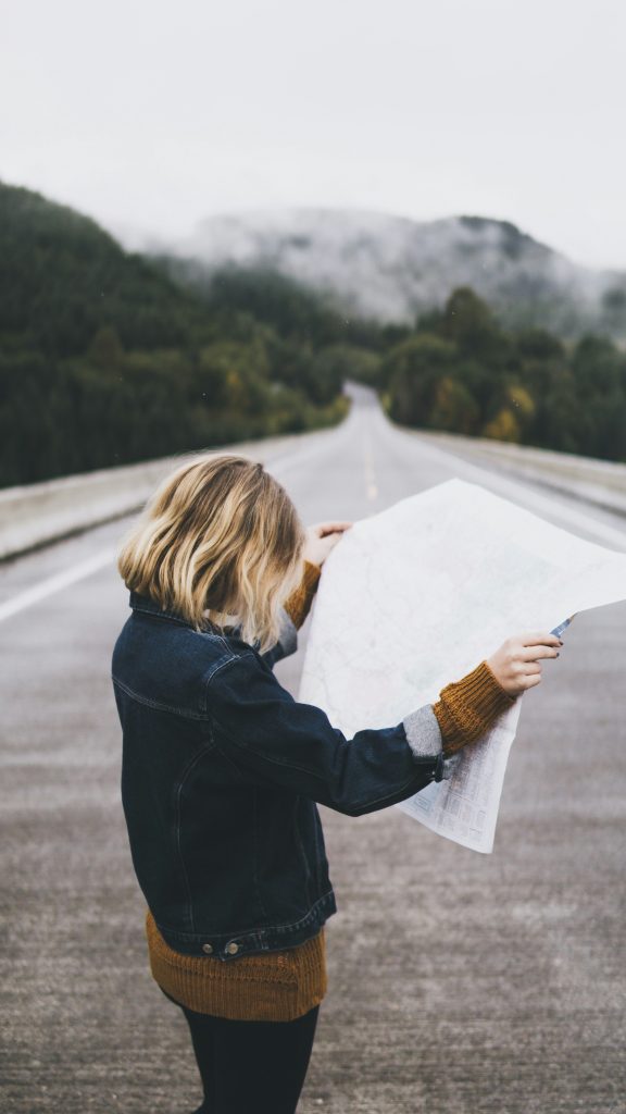 A woman is standing in a road holding open and looking at a roadmap